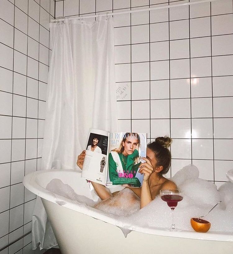 Person in a bathtub with a magazine and a cocktail, surrounded by bubbles.