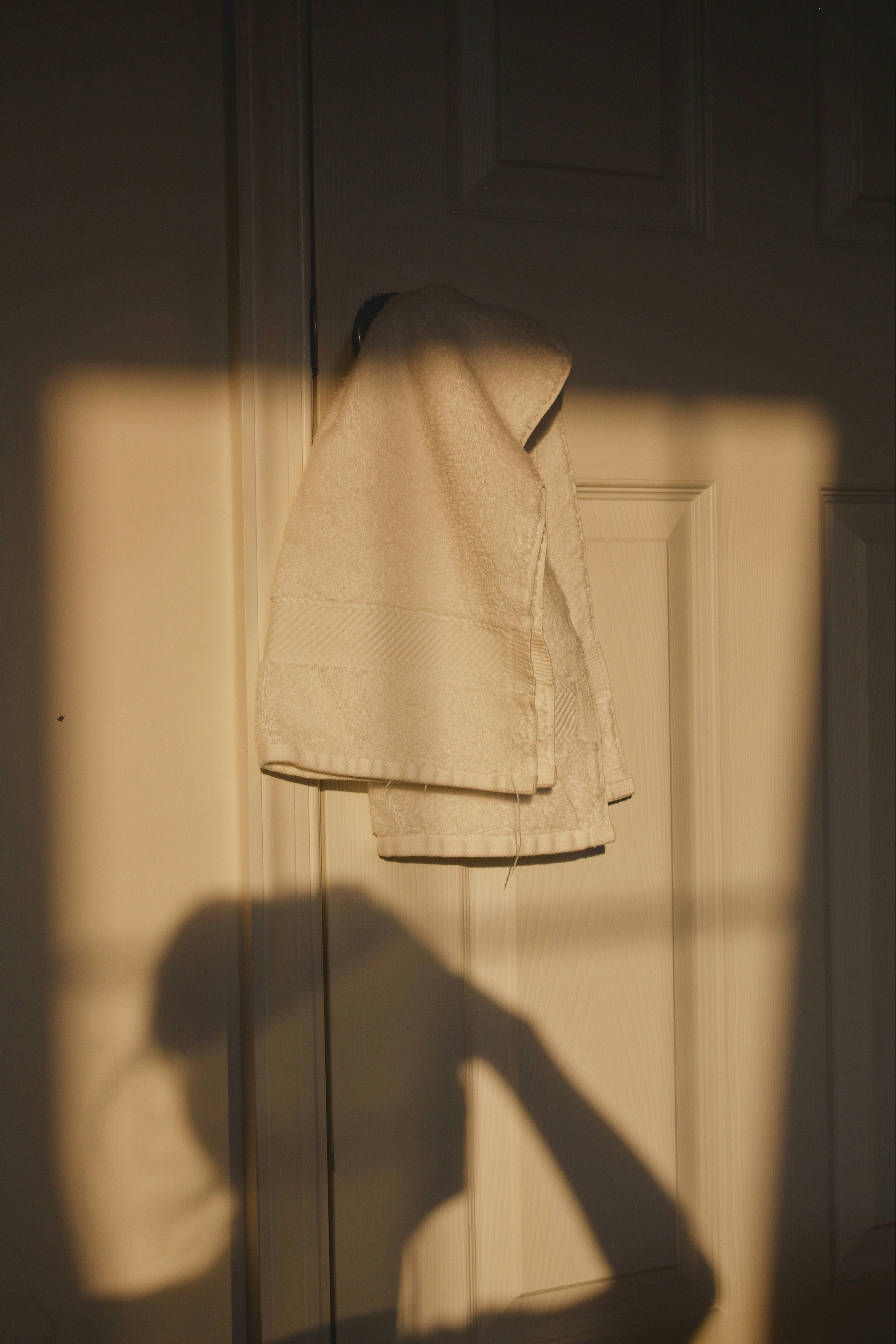 Light-colored towel hanging on a door with a shadow cast by a person taking the photo.
